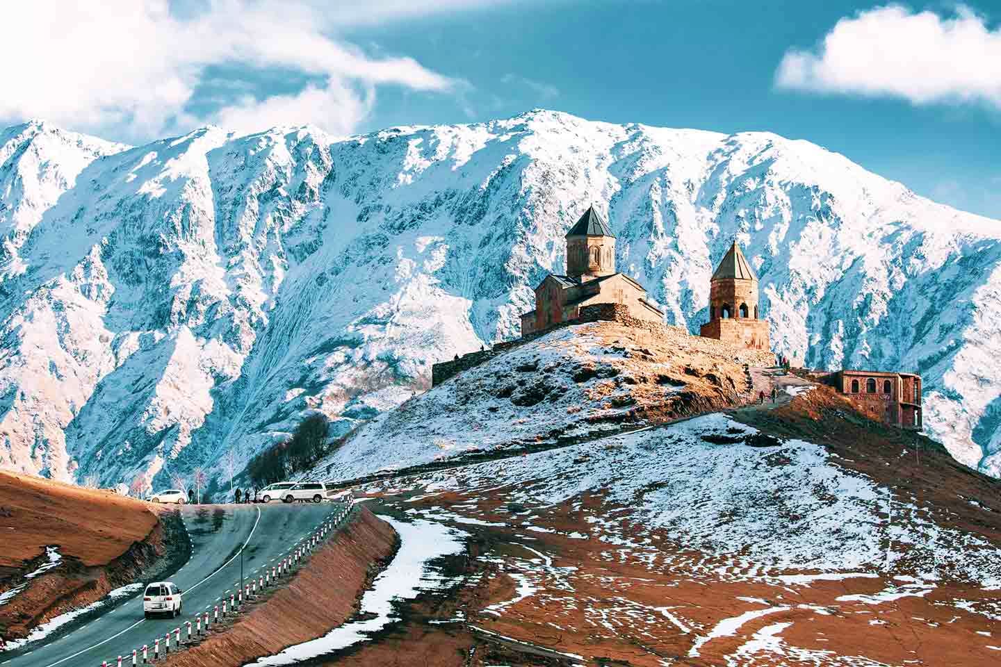 Snow-capped mountains with a historic Armenian church featuring twin spires on a hillside in Georgia